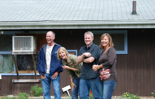 A group of people standing in front of a brown house