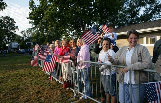 A group of people are standing behind a fence holding american flags.