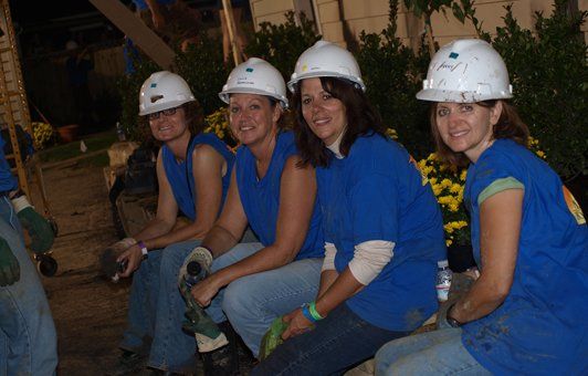 A group of women wearing hard hats are sitting on the ground