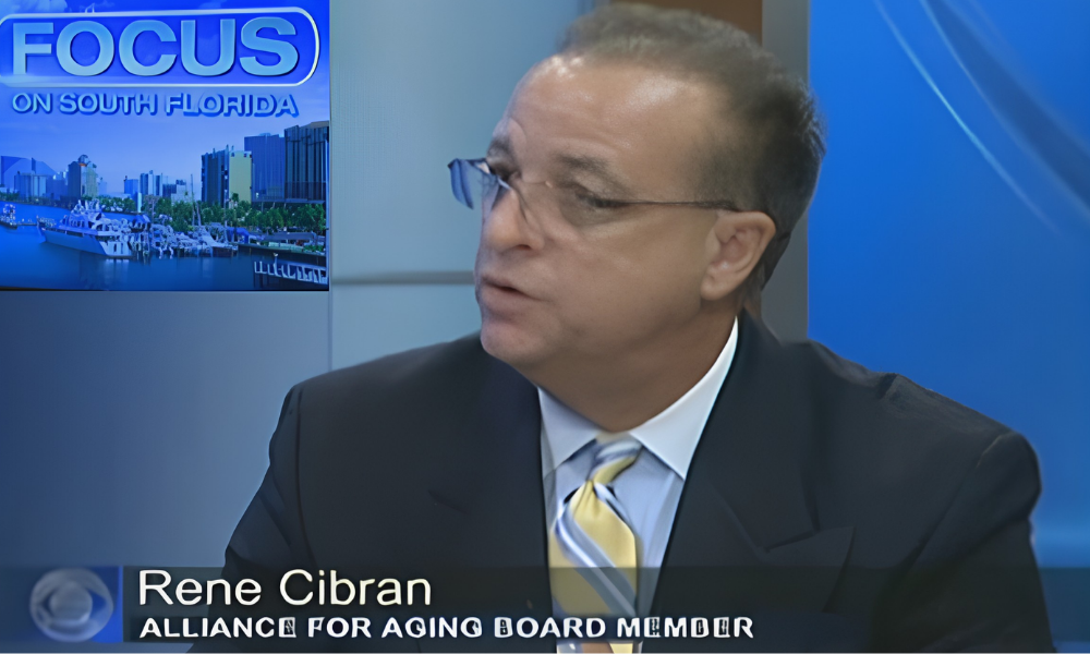 Man in suit and glasses speaking on a blue news set labeled “FOCUS”; lower third reads “Rene Cibran.”