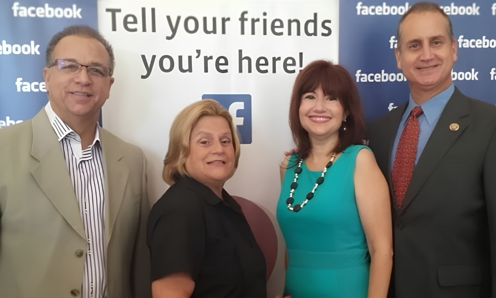Four people posing at a Facebook event backdrop reading “Tell your friends you’re here!”