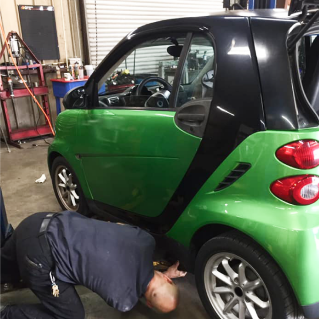 Mechanic working on car's differential, holding gear, wearing glasses, in shop. | Highlands Complete Auto