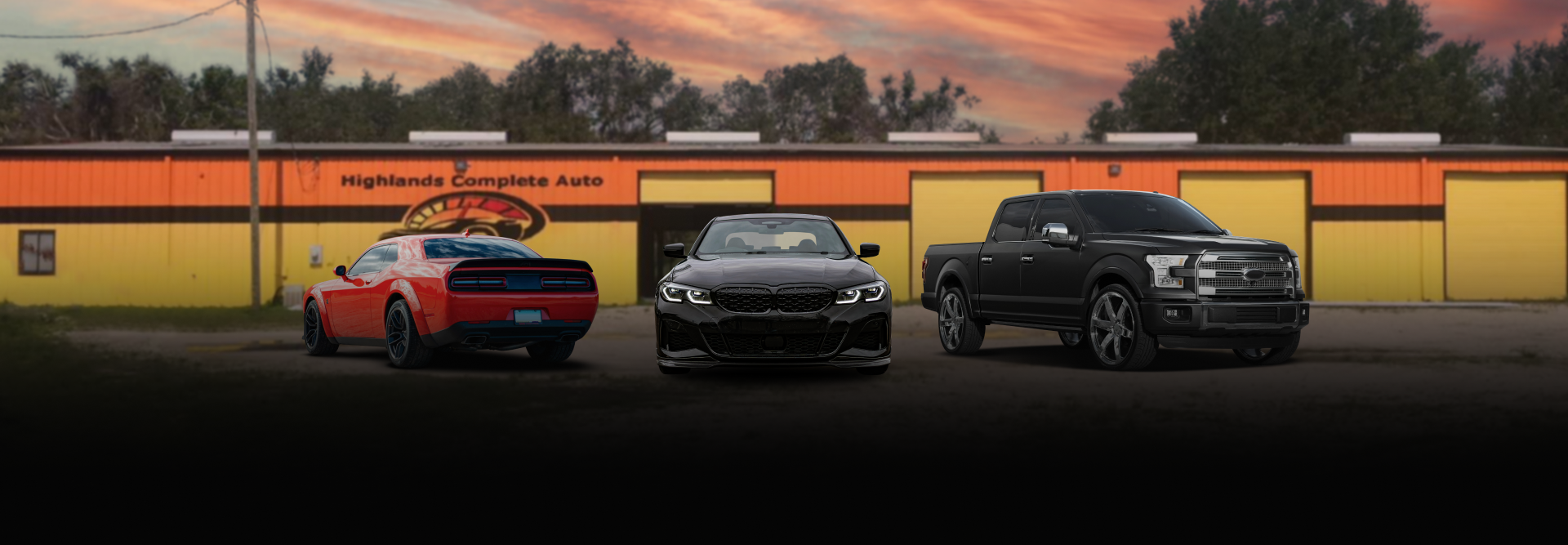 A red car and black truck parked outside a garage with yellow doors during sunset. | Highlands Complete Auto