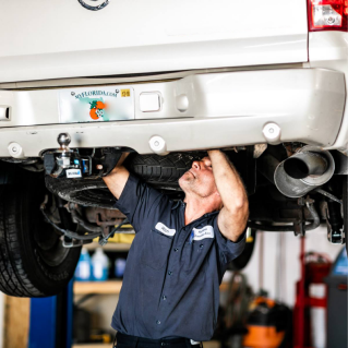 Mechanic working under a white truck, inspecting its undercarriage in a garage. | Highlands Complete Auto