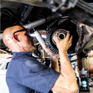 Mechanic working on car's differential, holding gear, wearing glasses, in shop. | Highlands Complete Auto