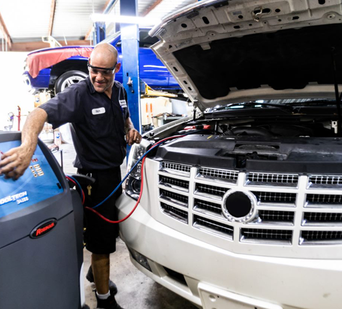 Mechanic servicing a white car's air conditioning system in a garage using a blue machine. | Highlands Complete Auto