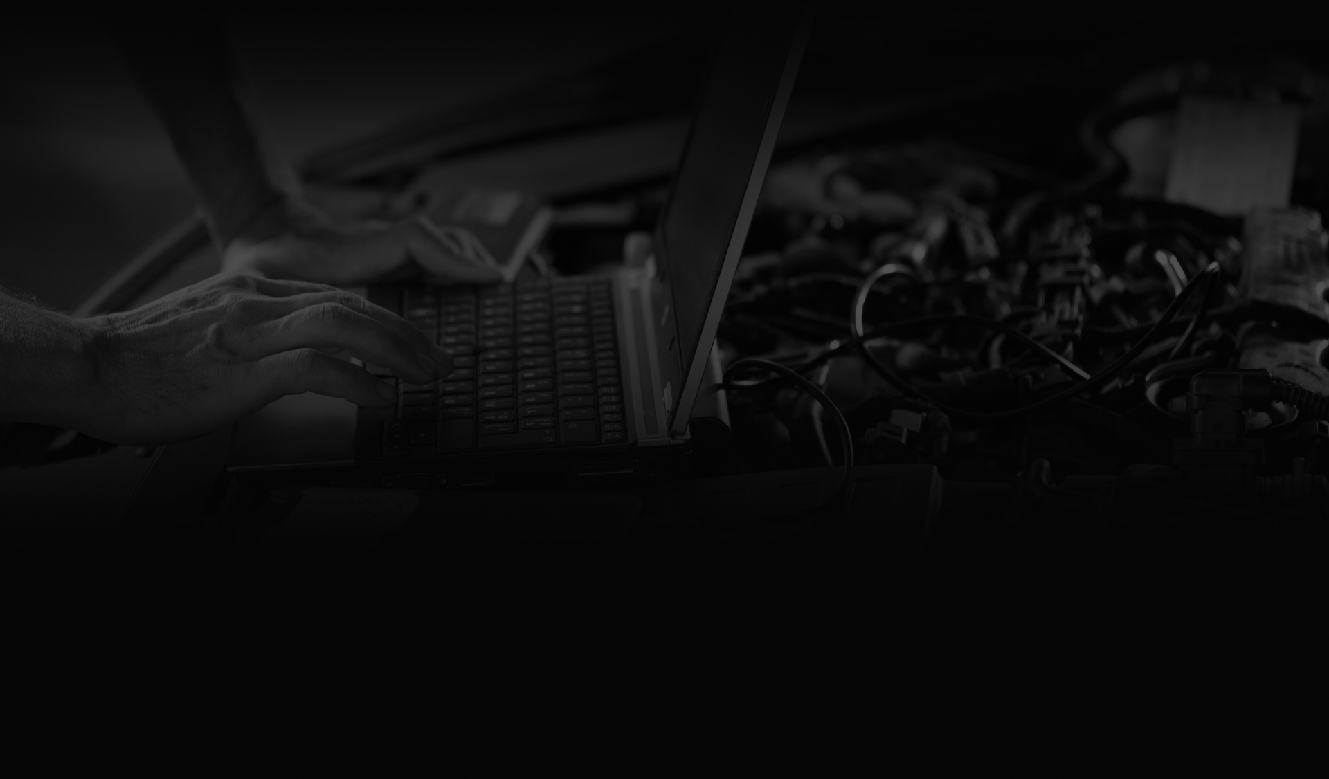 Hands typing on laptop keyboard, wires and other items in the background. | Highlands Complete Auto