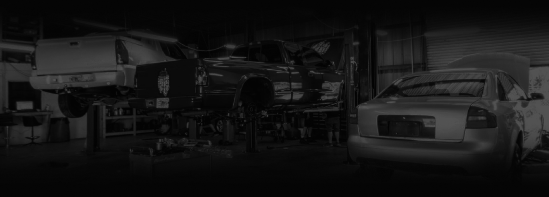 A car repair shop with a car on a lift and another car parked nearby. | Highlands Complete Auto