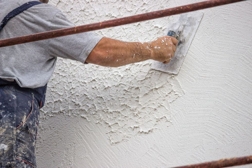 Persona che applica lo stucco su un muro usando una cazzuola.