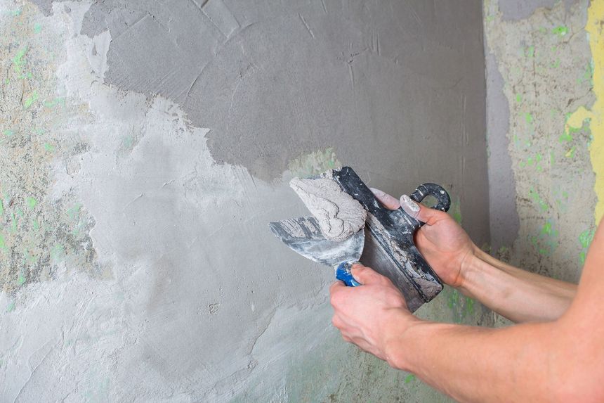 Persona che applica l'intonaco su un muro con una cazzuola, creando una finitura liscia.