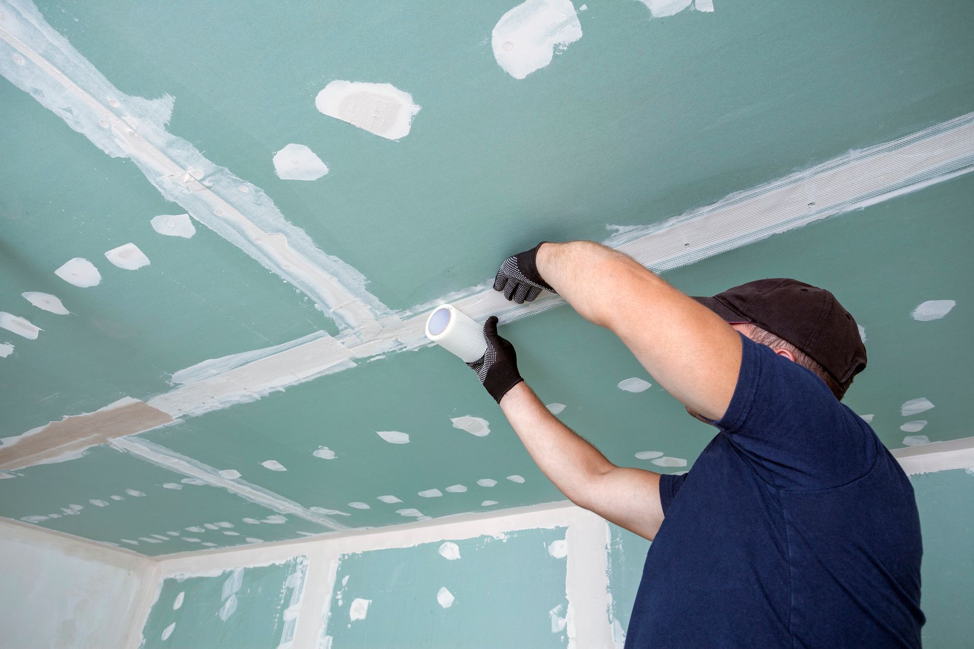 Persona che installa un controsoffitto con cartongesso verde e stucco bianco.