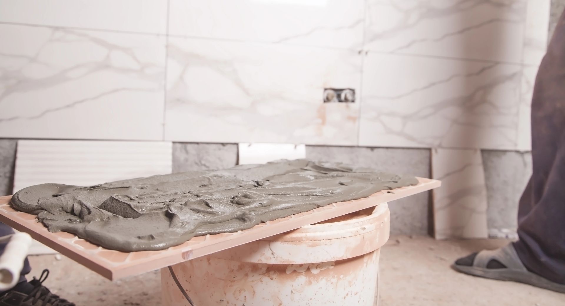 Piastrelle posate con malta su una tavola di legno, su un secchio, in un bagno in costruzione.