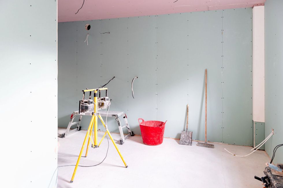Stanza in costruzione, con pareti verdi, soffitto rosa, attrezzi, un secchio rosso e cavi elettrici esposti.