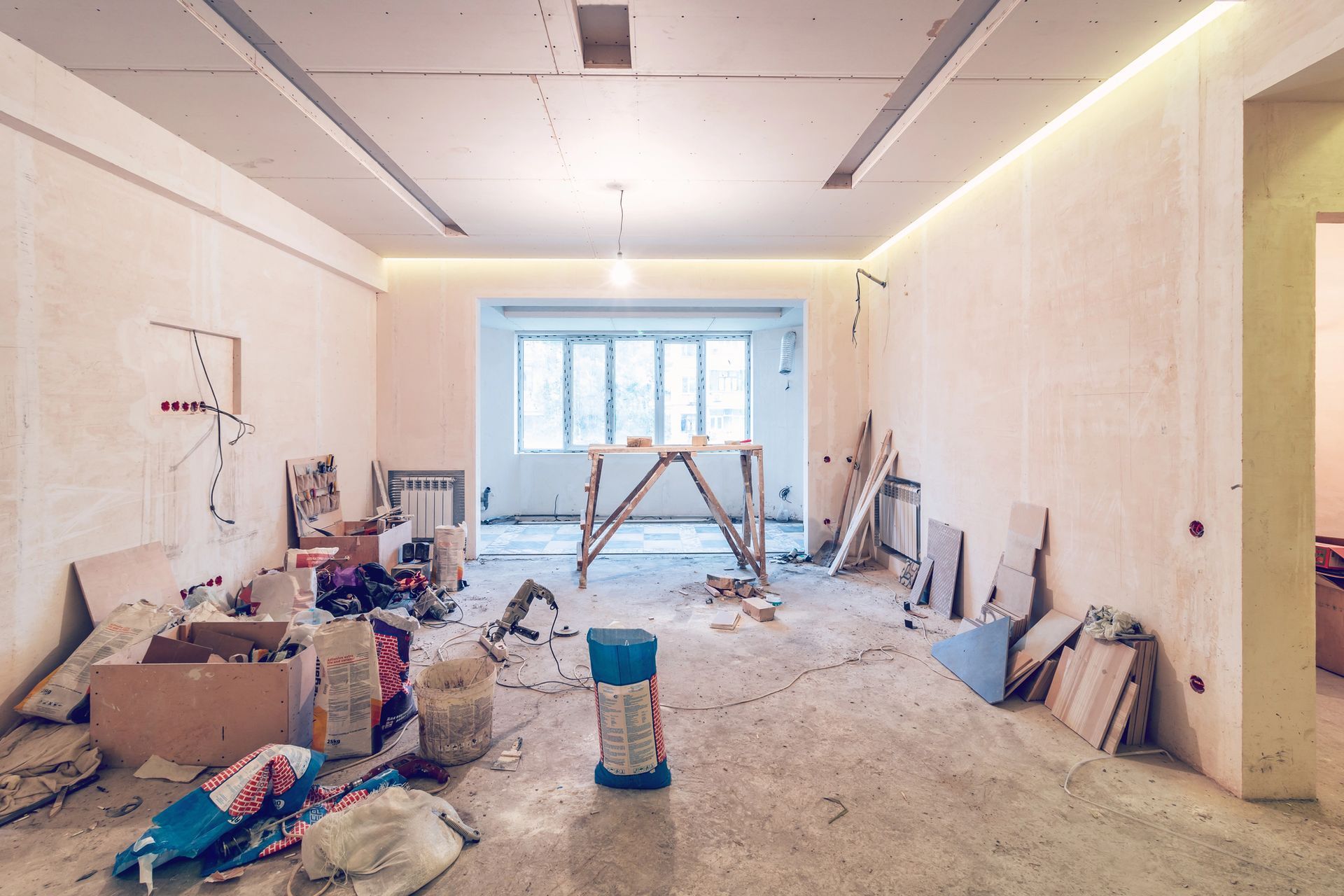 Stanza in fase di ristrutturazione con detriti sul pavimento, cartongesso e soffitto parzialmente rifinito.