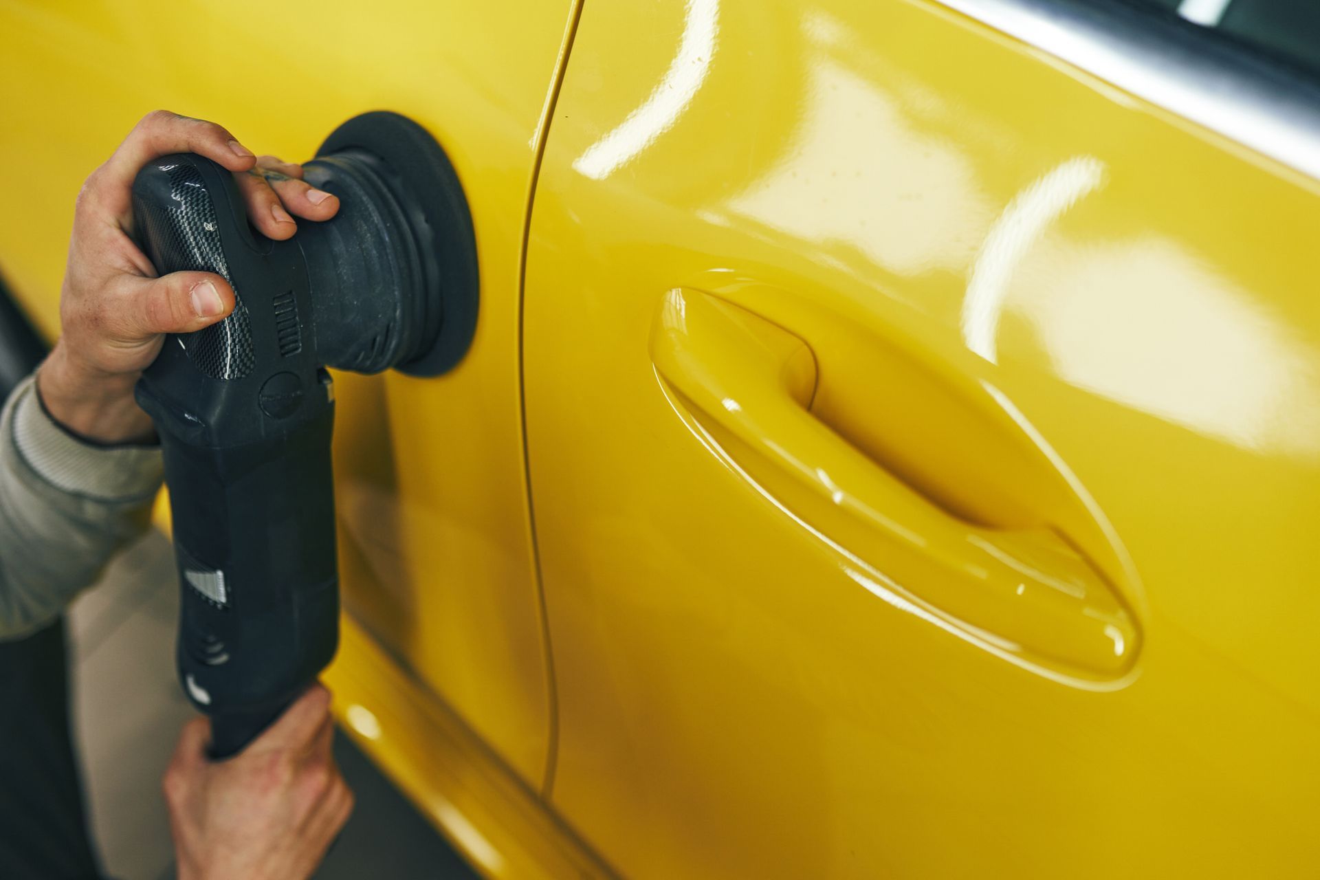 Person polishing a bright yellow car door with a black power polisher. Person polishing a bright yellow car door with a black power polisher.