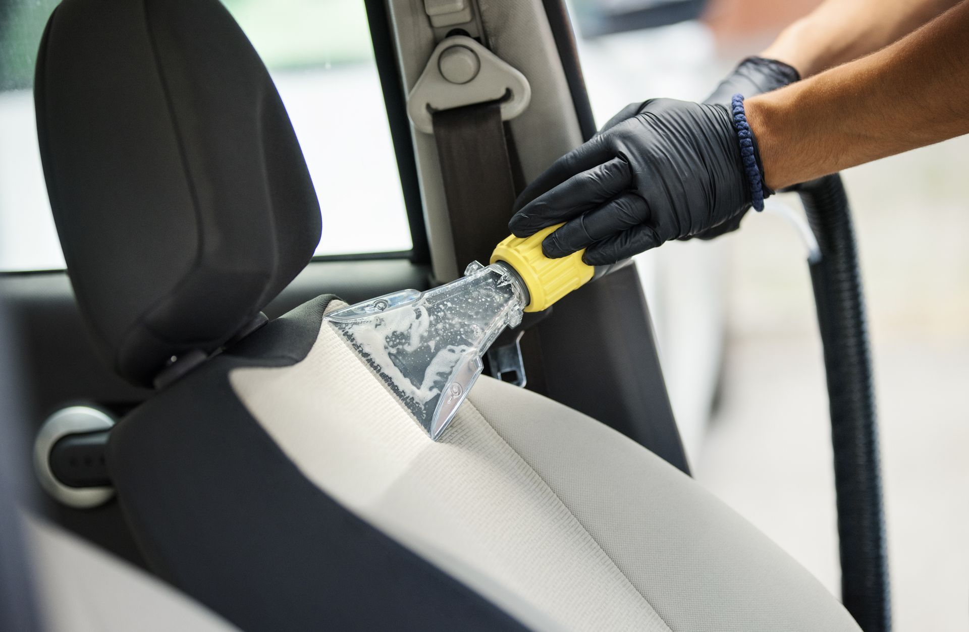 Person wearing black gloves cleaning a car seat with a handheld cleaning tool. Person wearing black gloves cleaning a car seat with a handheld cleaning tool.