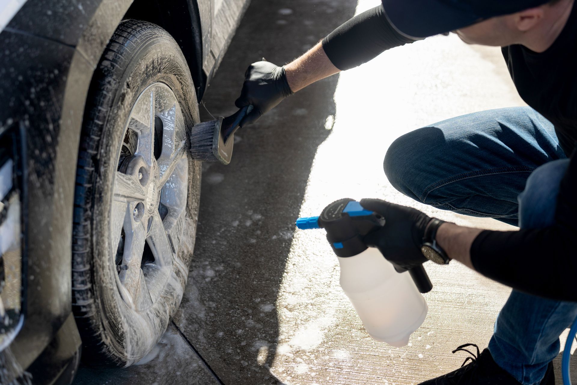 Person using a brush and spray bottle to clean a car tire with foam.