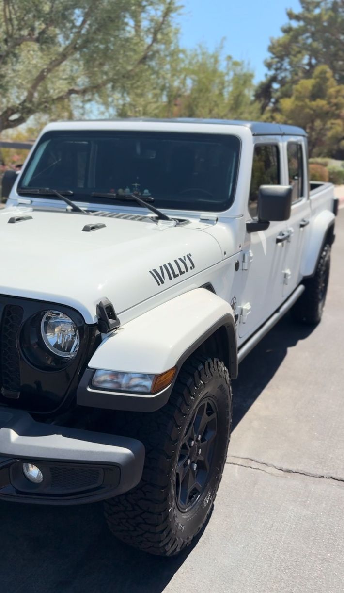 Man polishing a black car in a garage with a red light, using a rag and a spray gun.