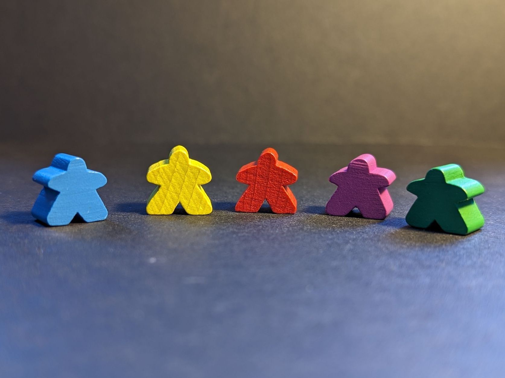5 meeples of different colors in a row, on a black background