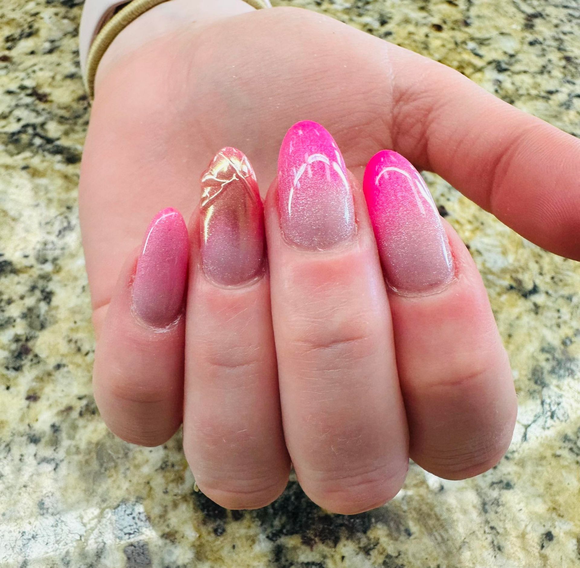 Hand with long pink ombré manicured nails on a granite countertop