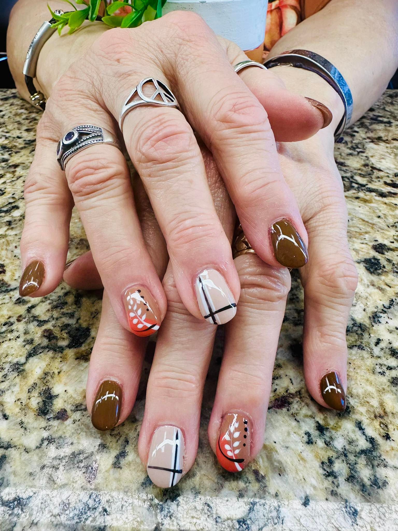 Hands with patterned nail art and rings resting on a speckled countertop.