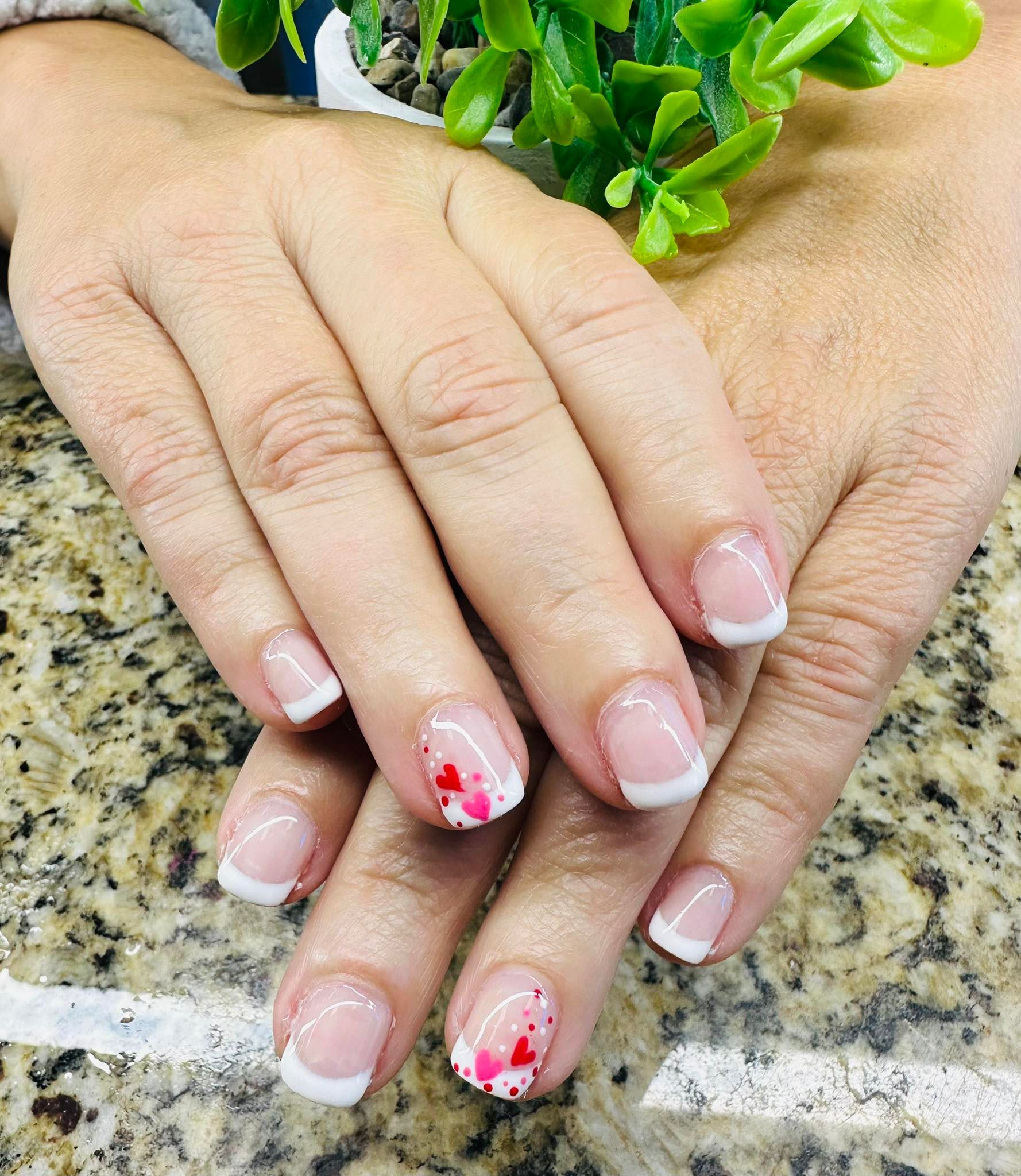 Hands with French manicure and red floral nail art resting on a granite countertop near a green plant