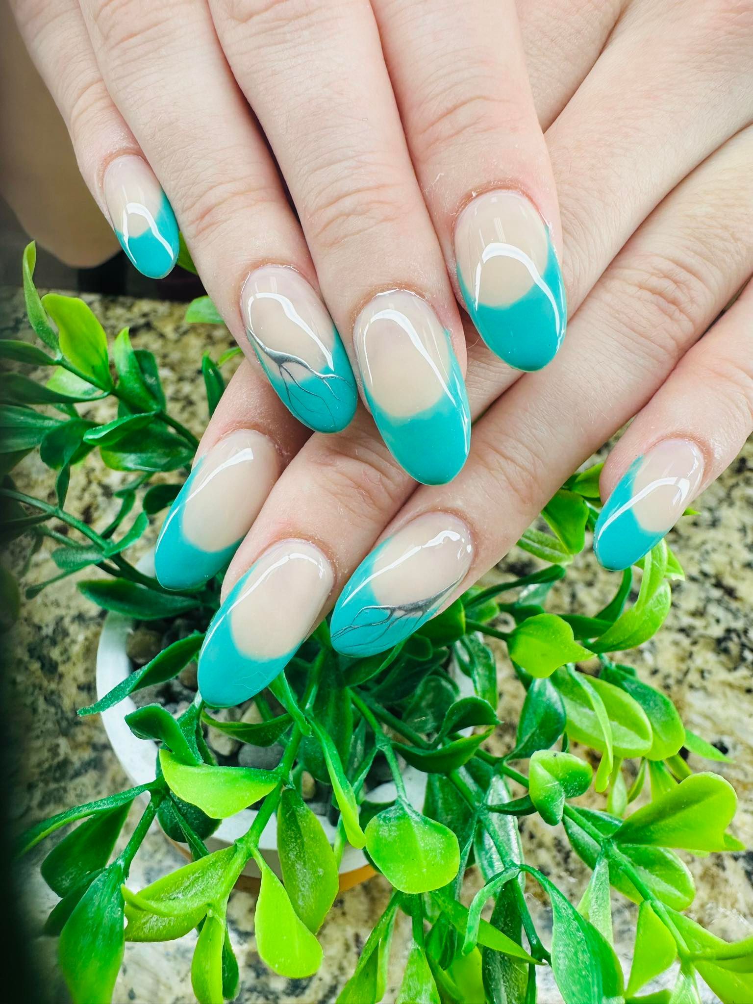 Hands with turquoise French manicure resting on green leaves.