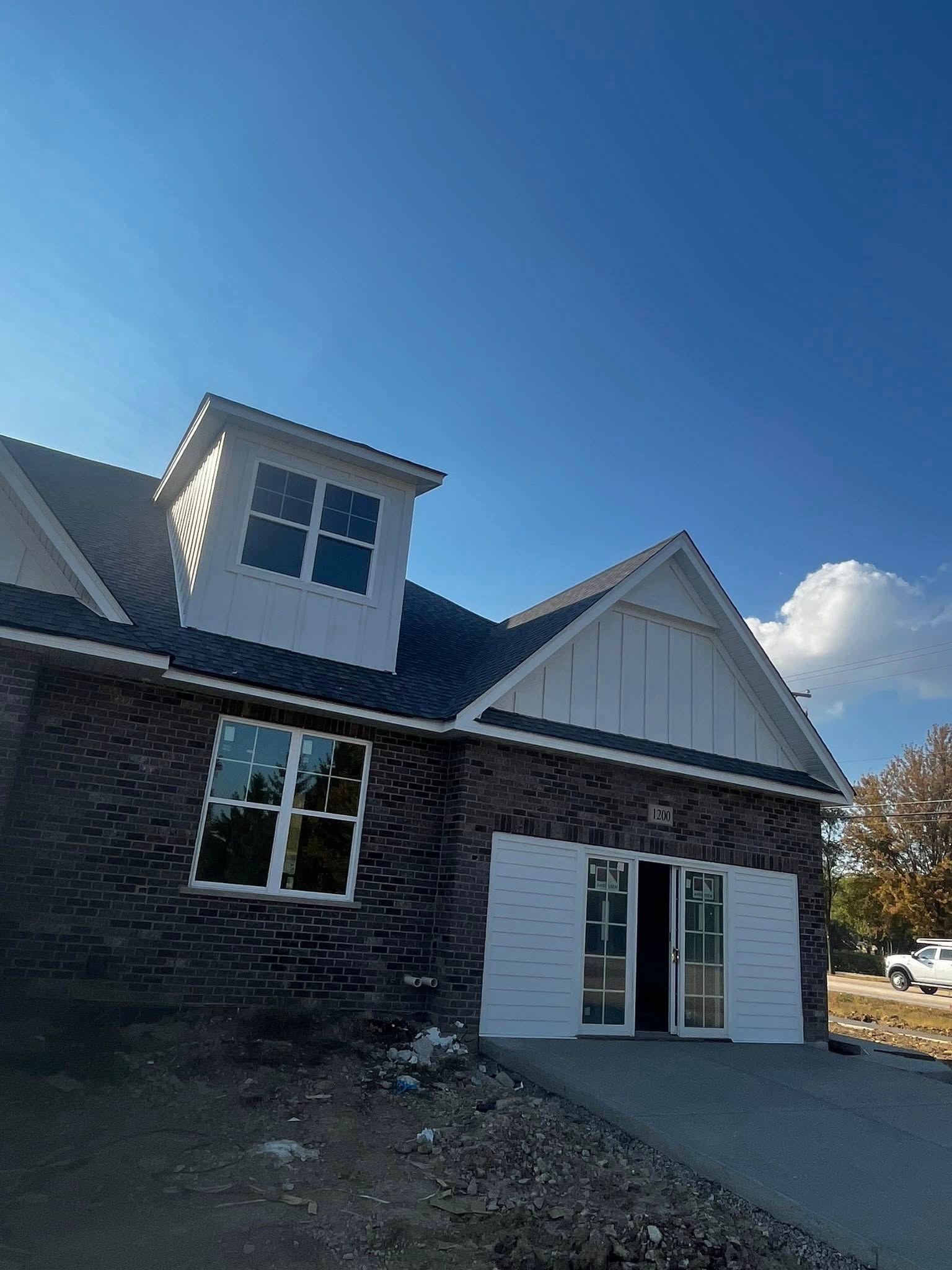 A brick house exterior under a blue sky, featuring a dormer window, a white gable, and a partially installed garage door.