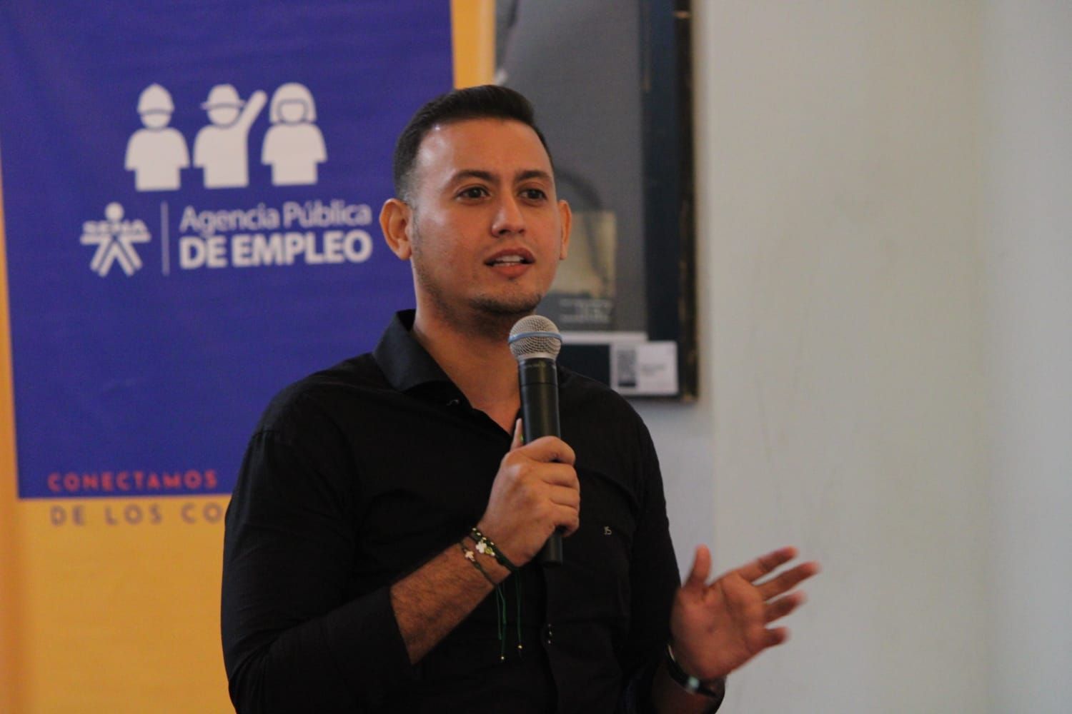 Un hombre sostiene un micrófono frente a un cartel que dice atención pública de empleo.