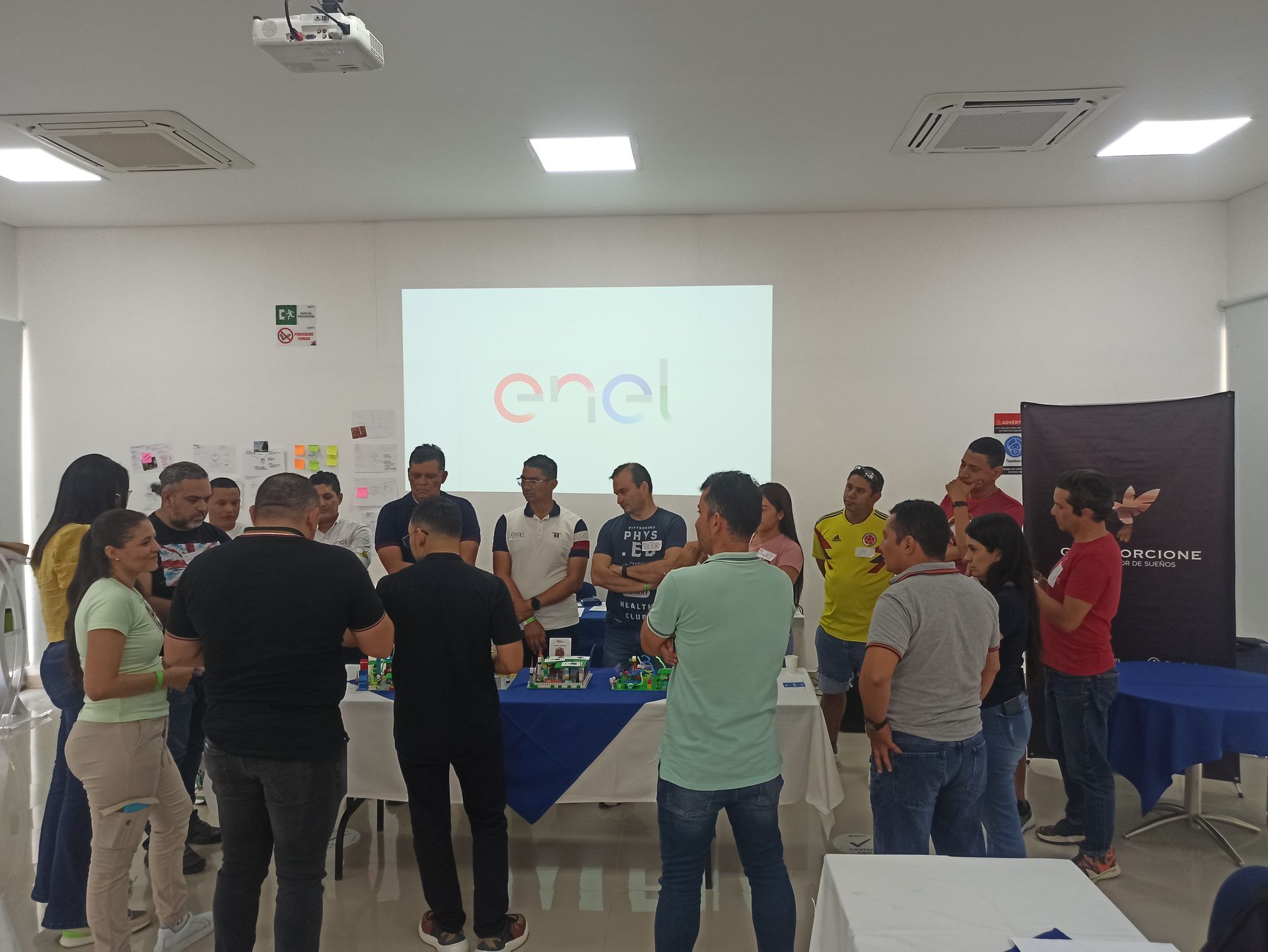 Un grupo de personas está de pie alrededor de una mesa frente a una pantalla de proyector que dice enel.