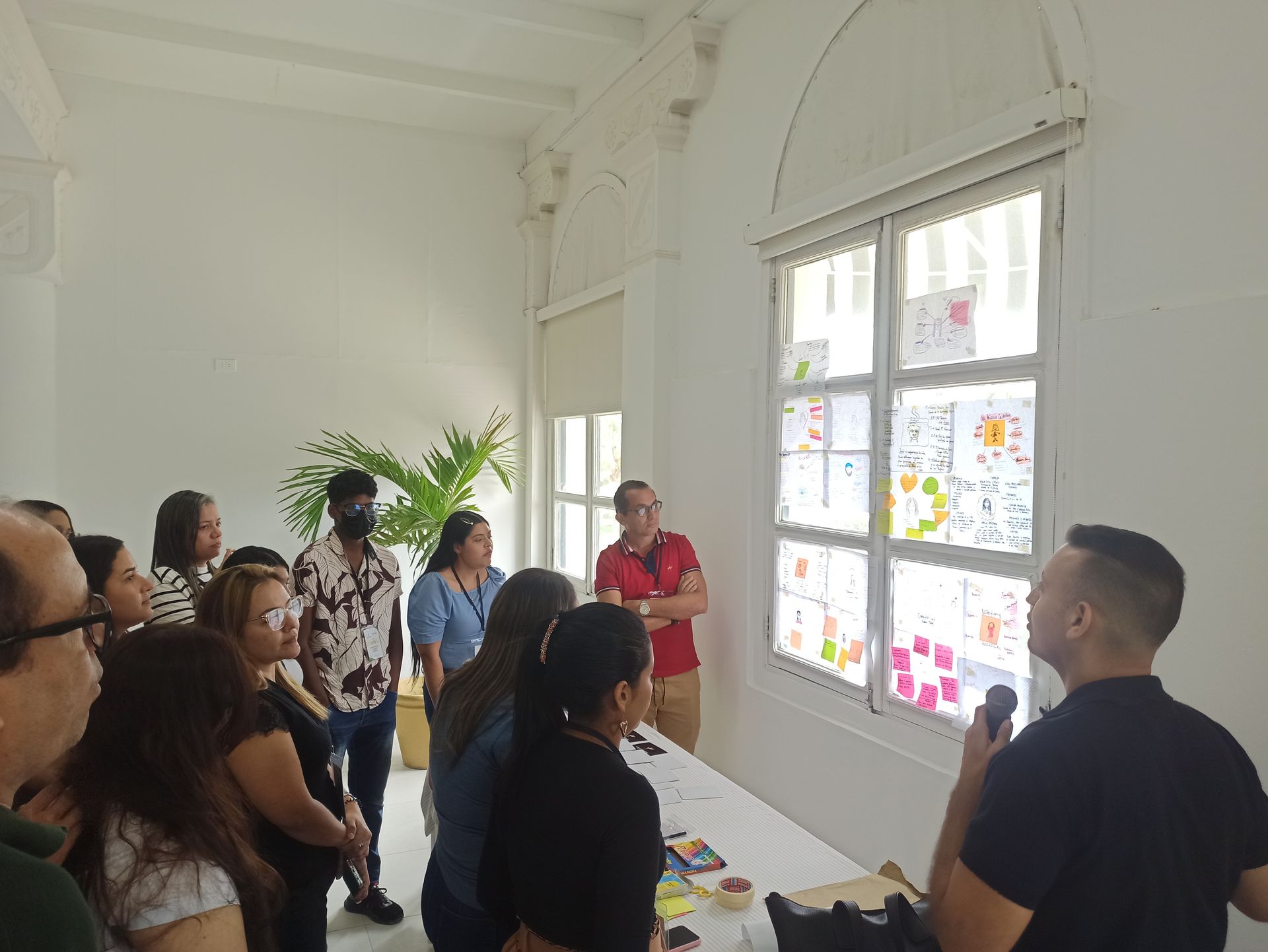 Un grupo de personas está de pie alrededor de una mesa frente a una ventana.