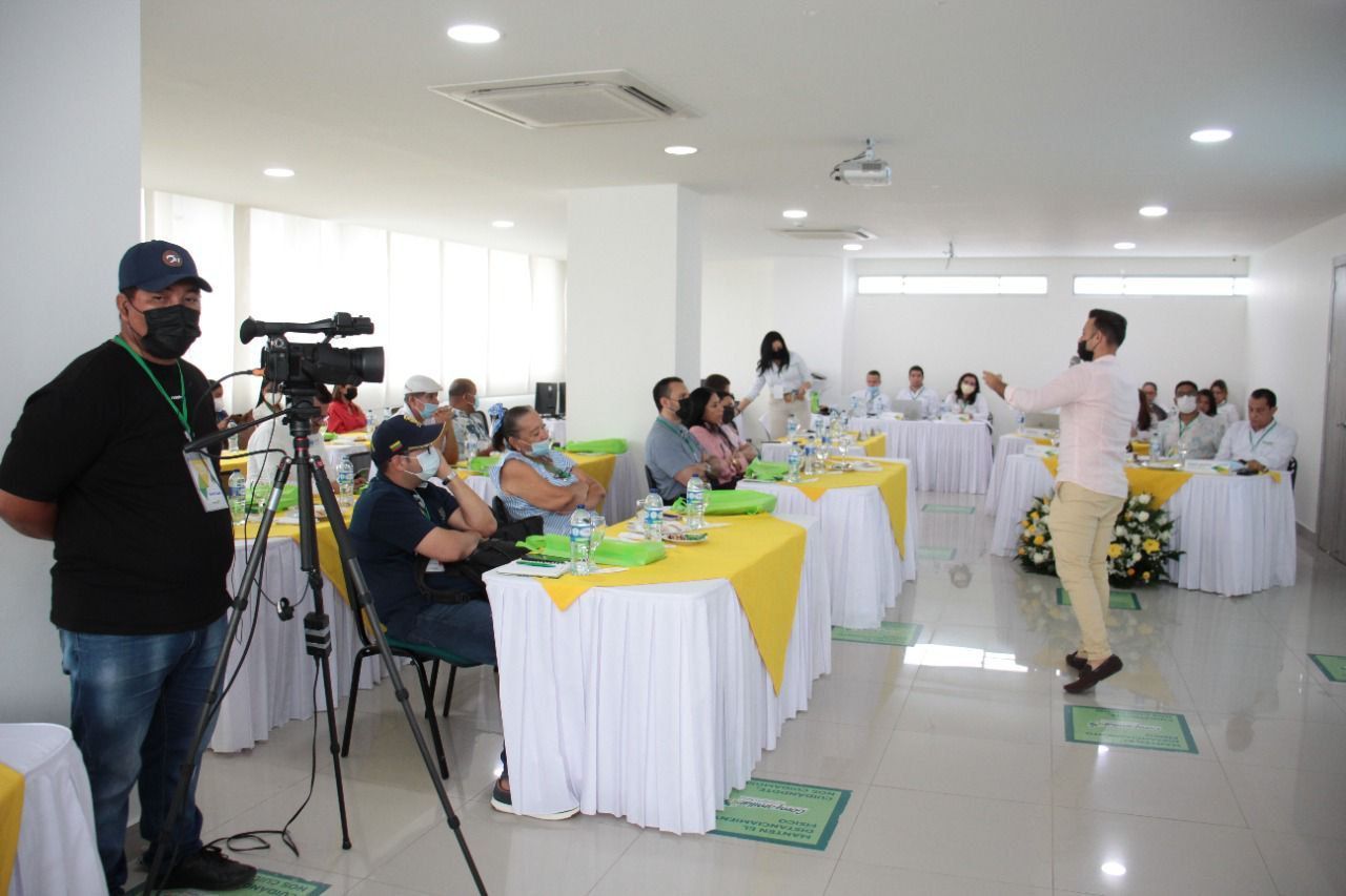 Un hombre está de pie frente a un grupo de personas sentadas en mesas.