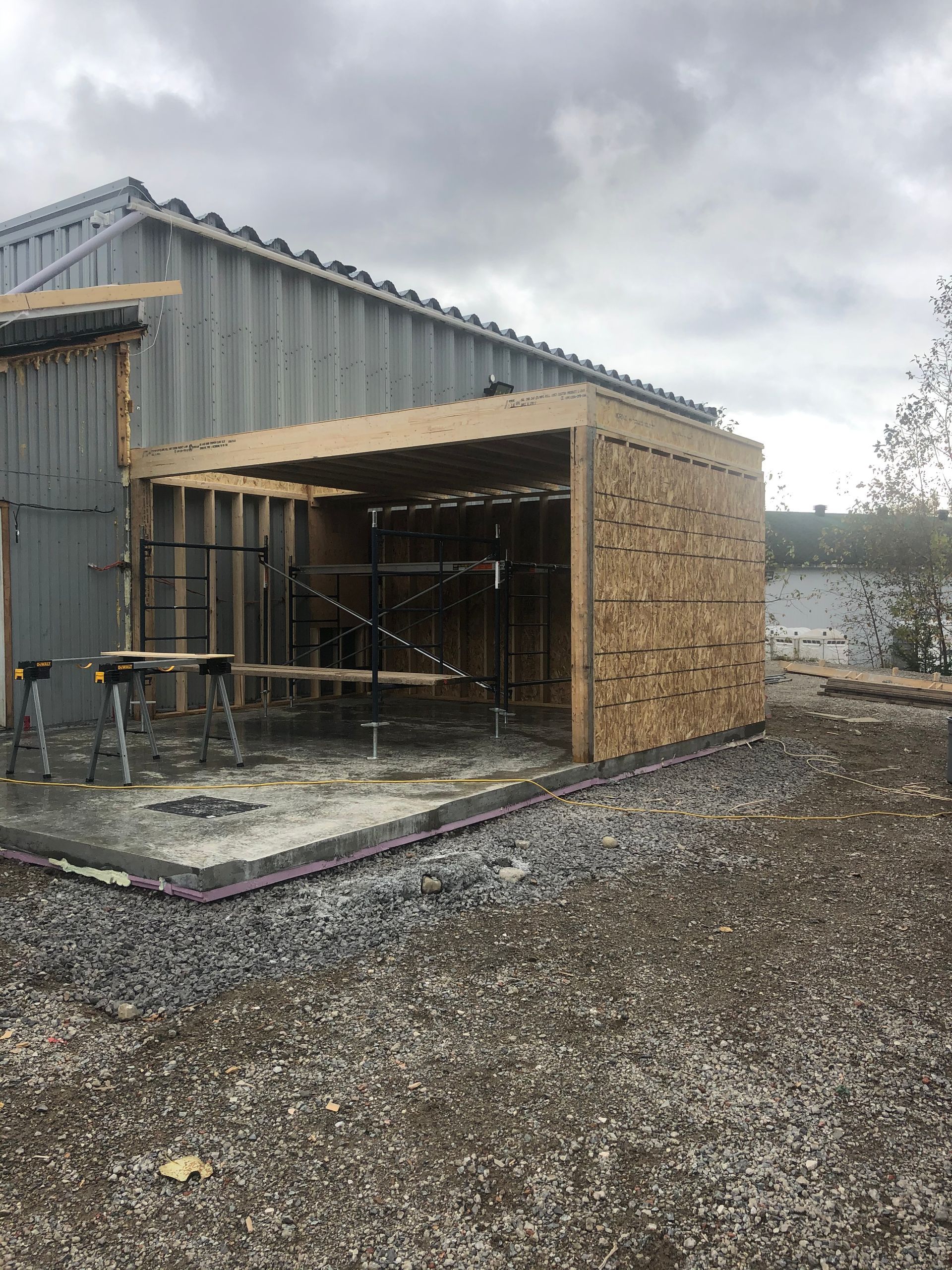 Un hangar est en cours de construction dans une zone de gravier à côté d'un bâtiment.