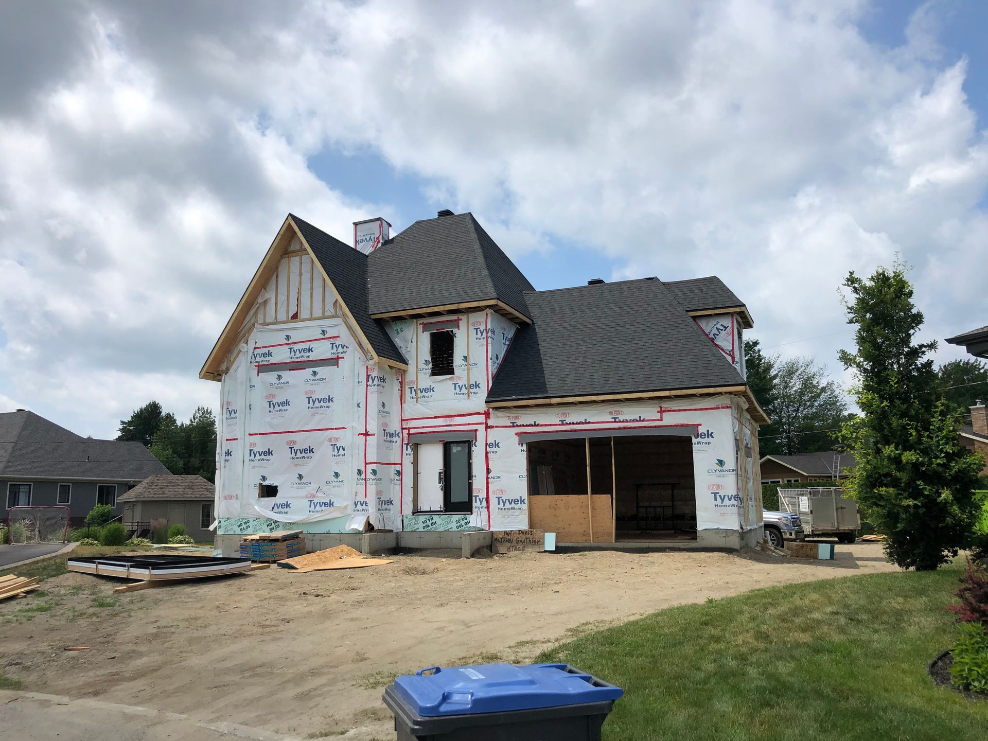 Une maison est en construction dans un quartier résidentiel avec une poubelle bleue devant elle.