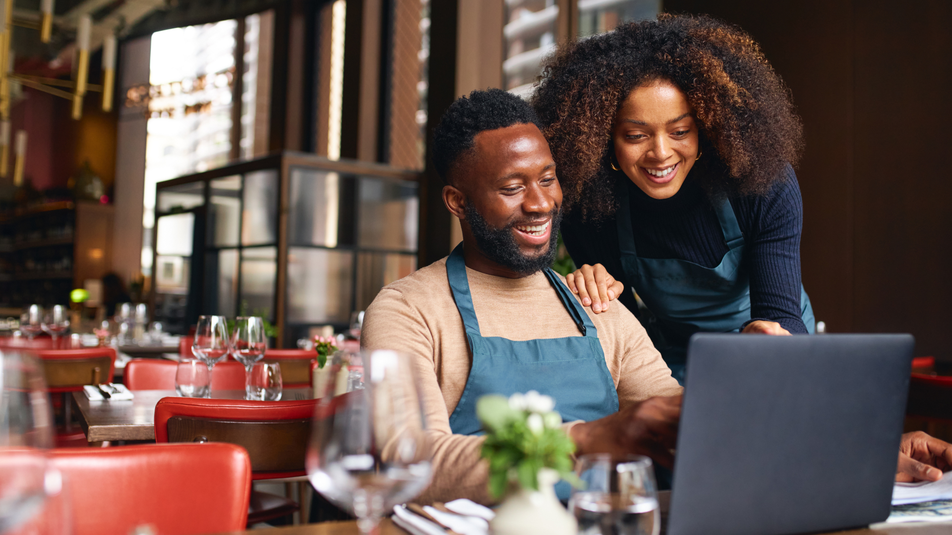 A man and a woman are looking at a laptop in a restaurant.