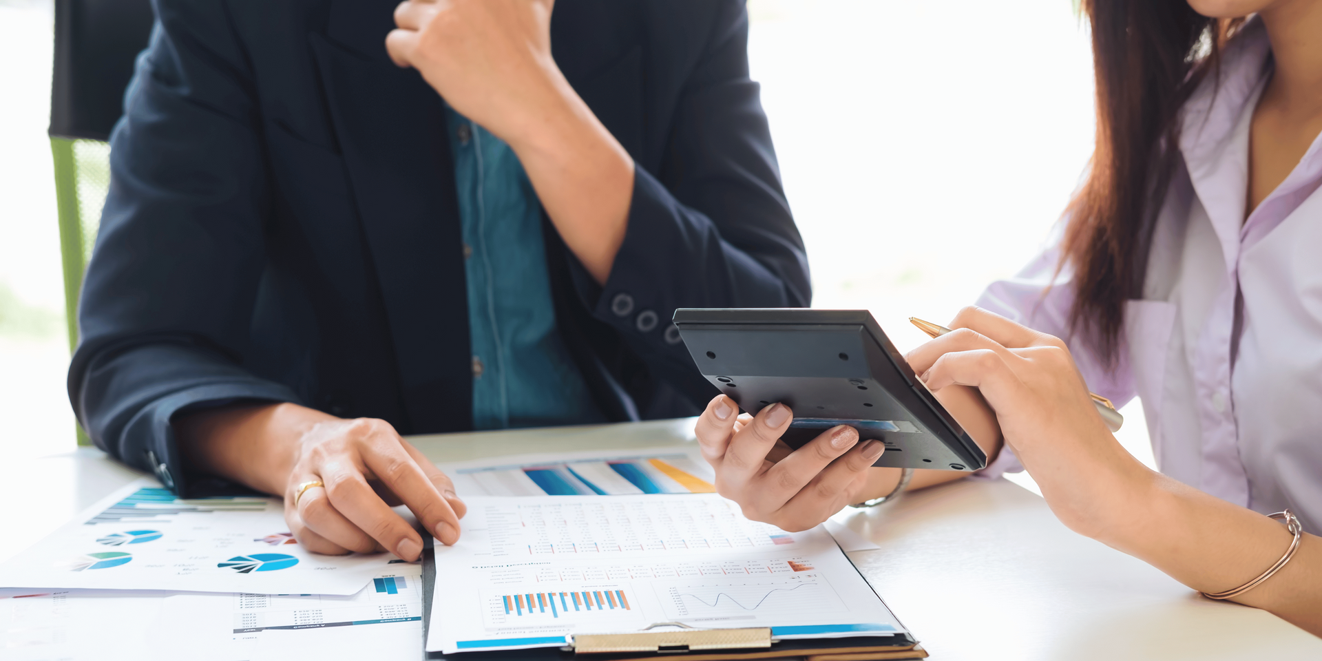 A man and a woman are sitting at a table looking at a calculator.