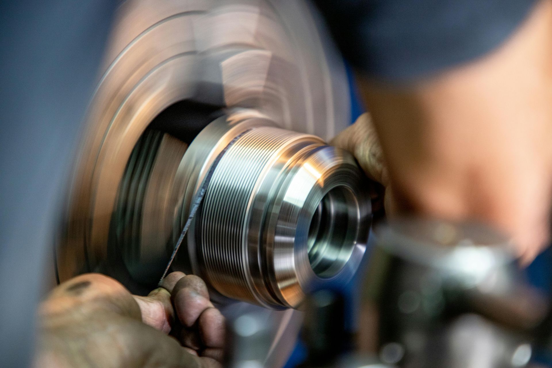A close-up of hands using a hand file to smooth a metallic part spinning on an industrial lathe.