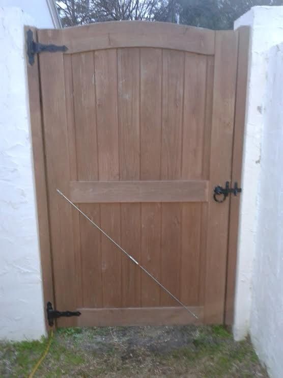 Wooden gate with black hinges and latch between white stucco walls