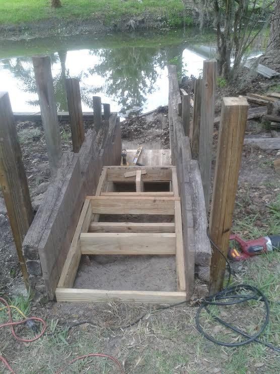Wooden staircase under construction leading down to a dock by a pond, with tools nearby