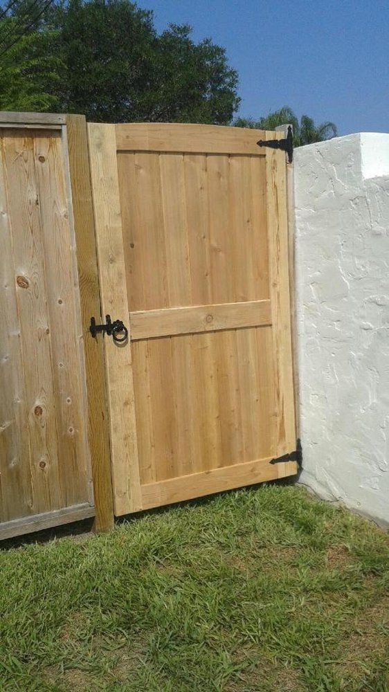 Wooden garden gate with black hinges, beside a white wall and grass lawn under a blue sky.