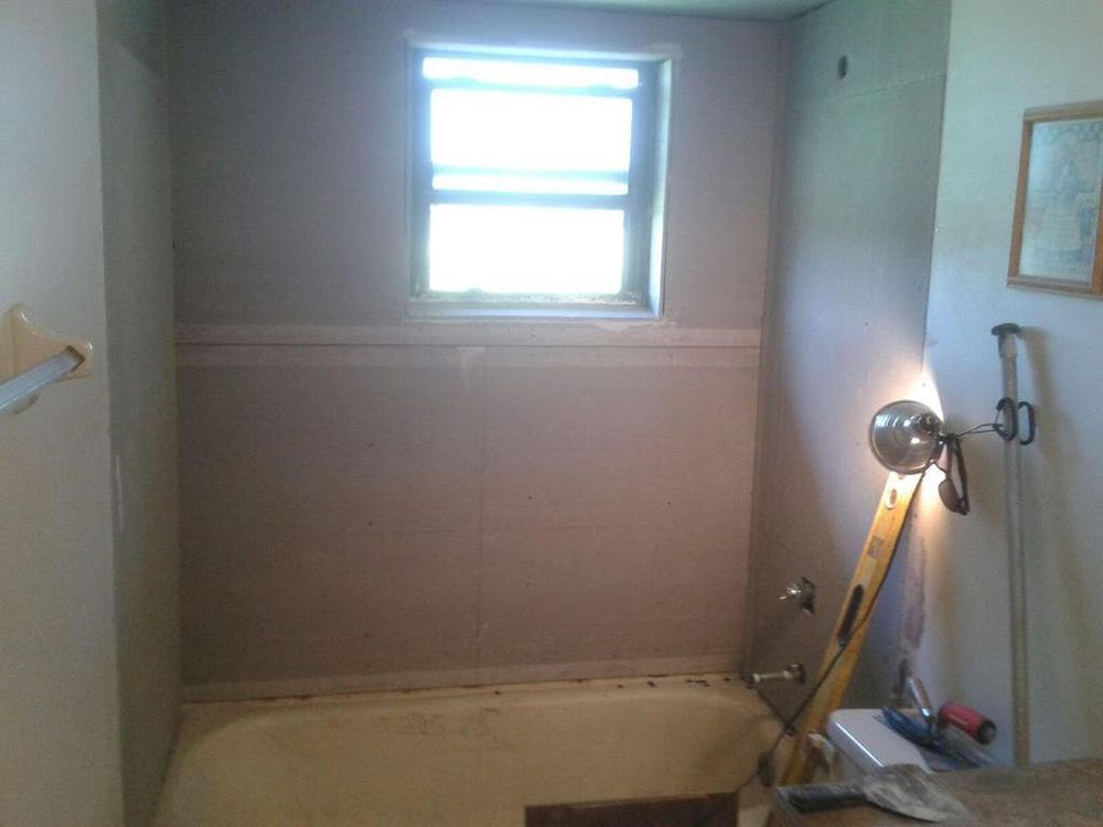 Small bathroom with a bathtub, window, and ladder leaning against the wall.