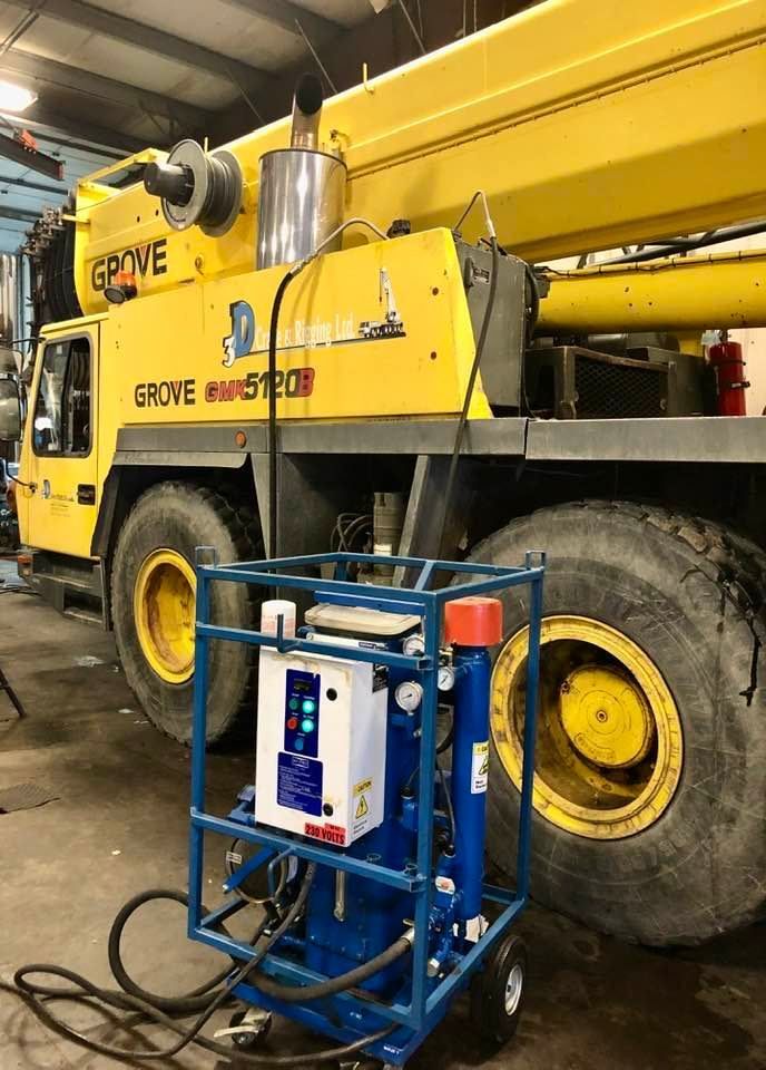 A yellow crane is parked in a garage with a cart attached to it.