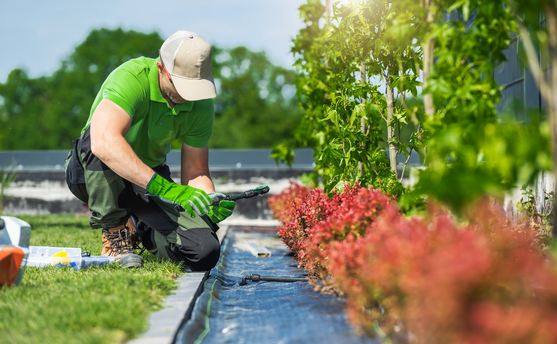 A man in a green shirt is kneeling down in a garden.