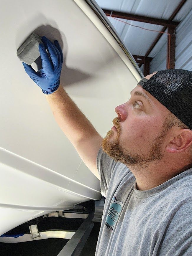 A person wearing a black hat and blue gloves cleans the chrome spokes of a car wheel.