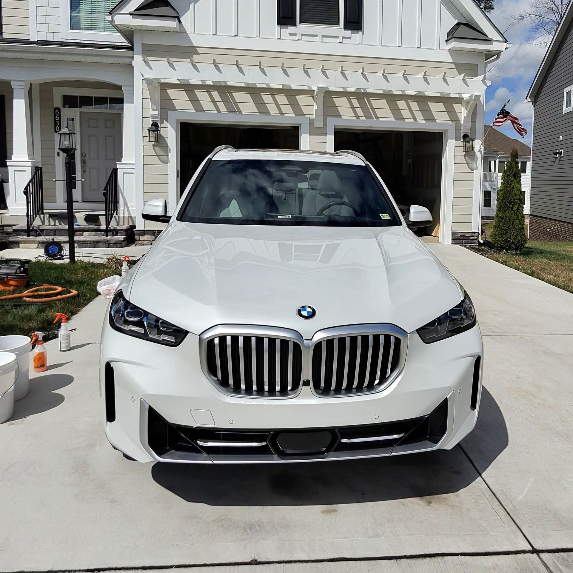 White BMW SUV parked in front of a house with a two-car garage.