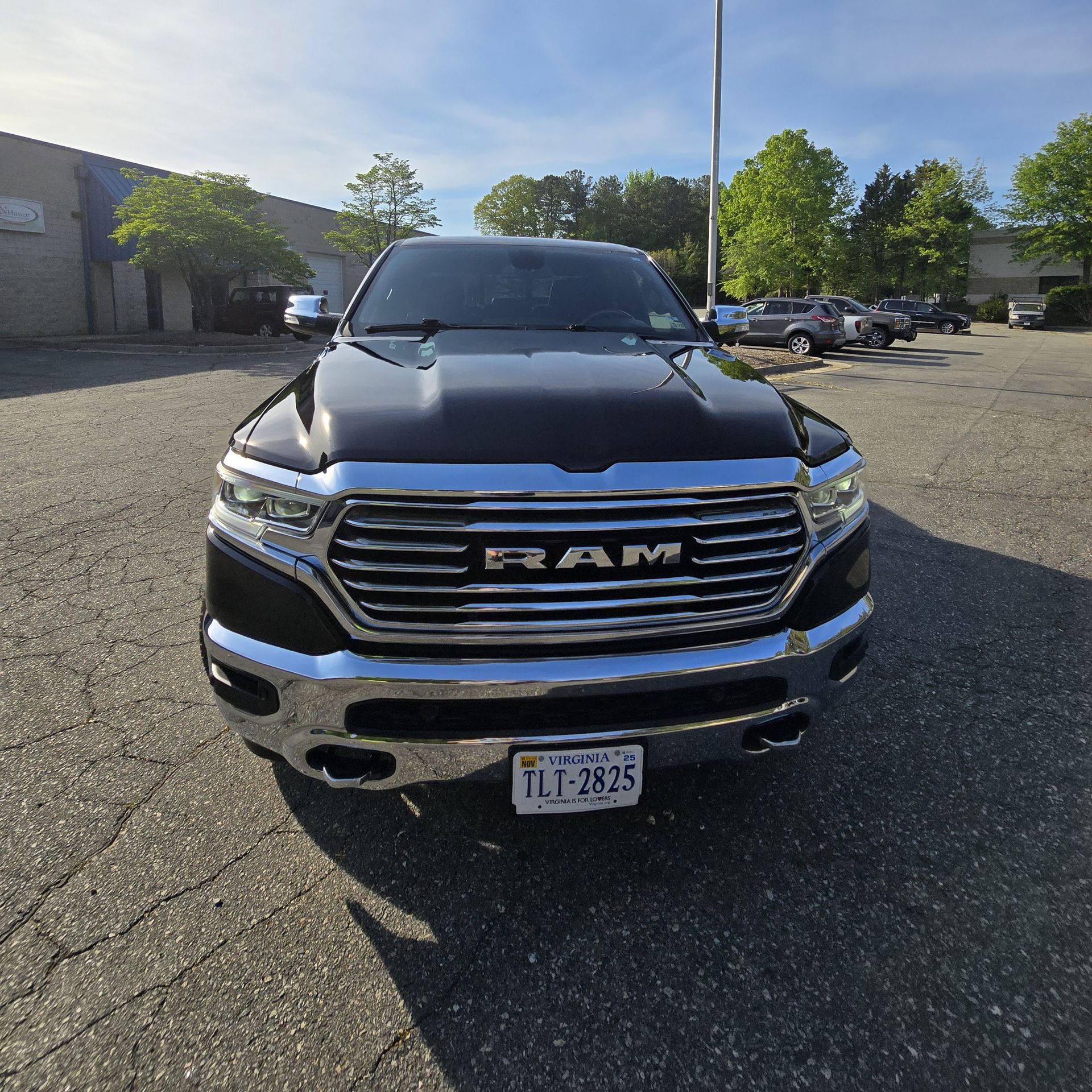 Black RAM pickup truck, chrome grille, parked in a lot. Blue sky.