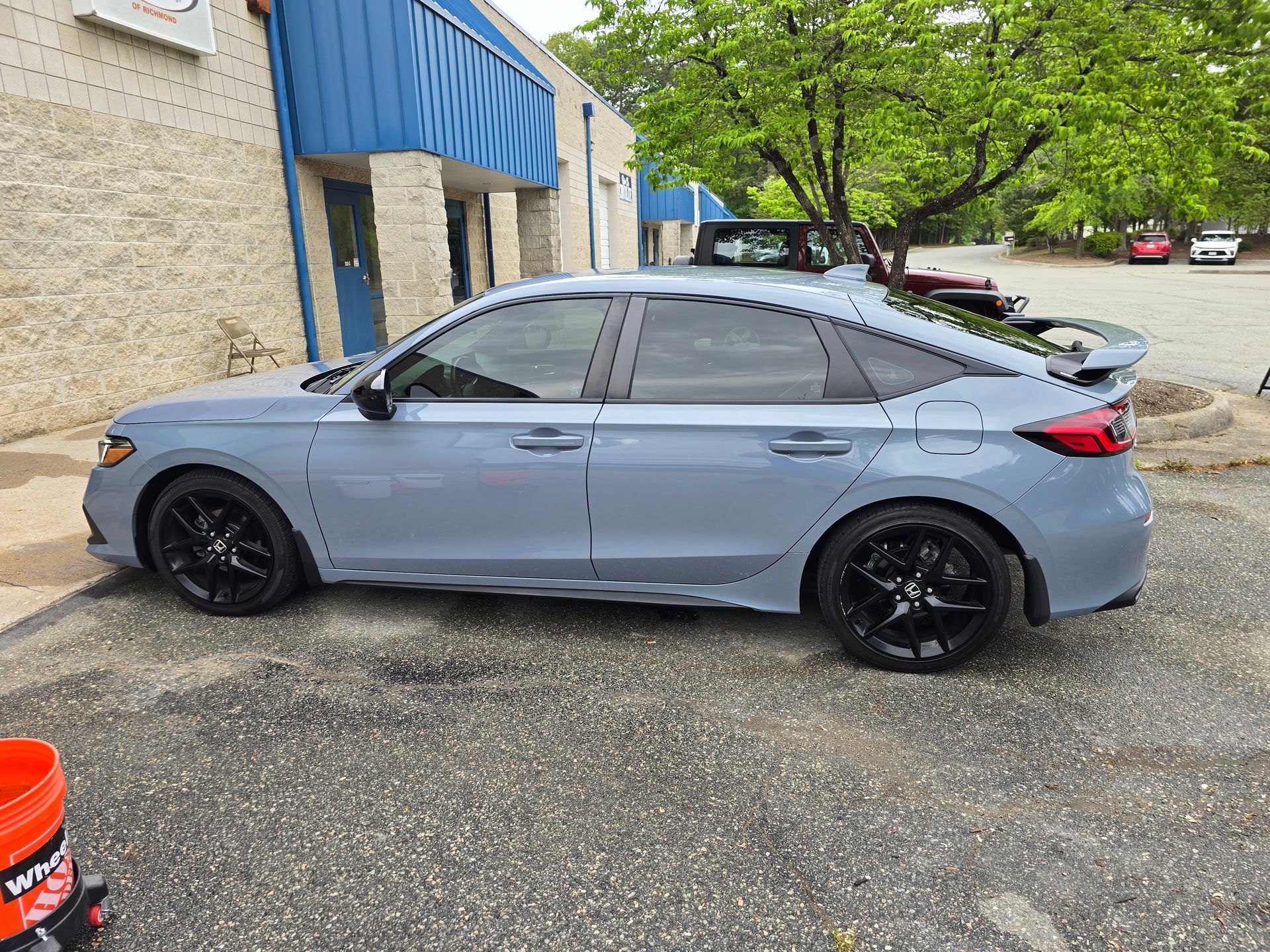 Blue Honda Civic hatchback with black wheels parked near a building.