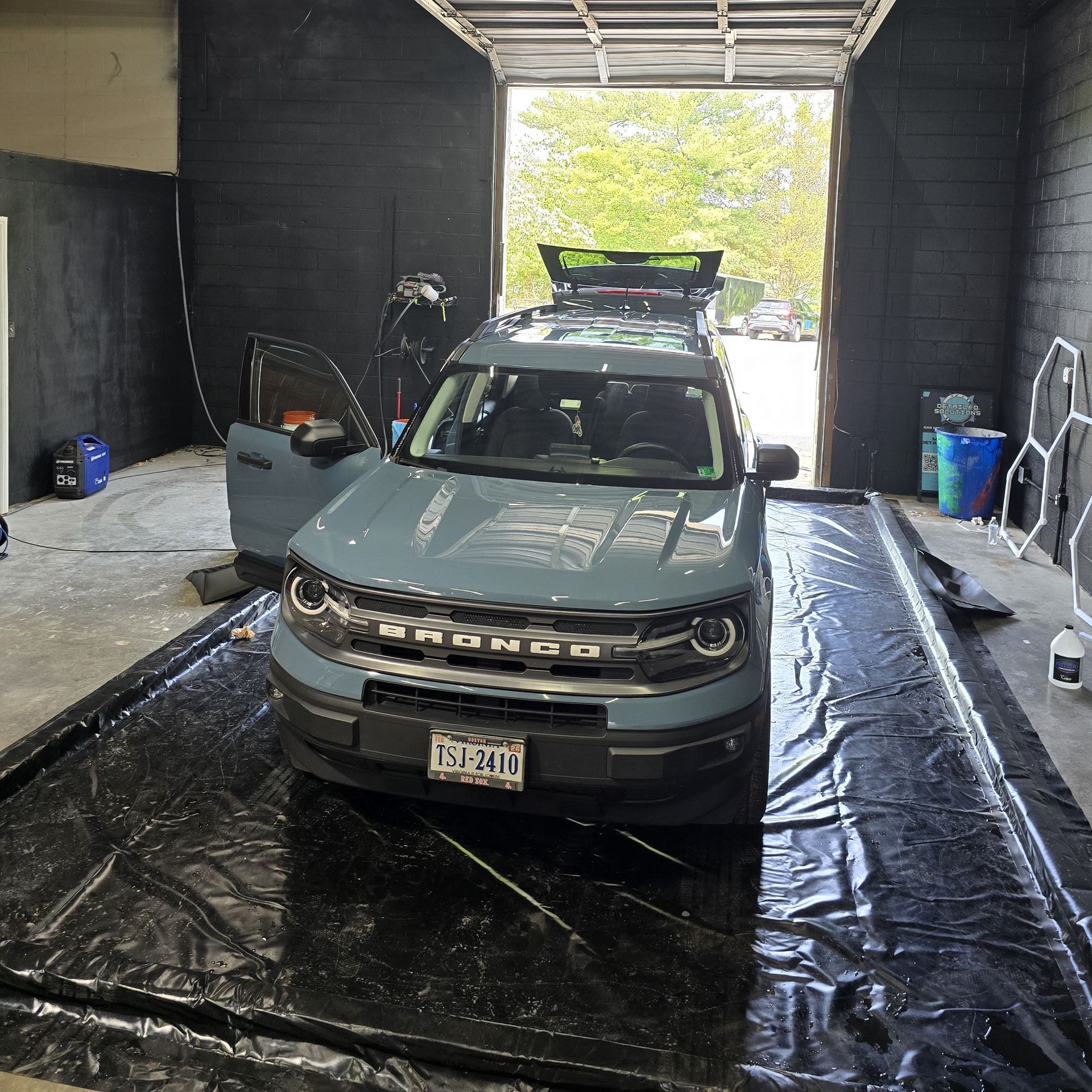 Blue Ford Bronco Sport in a car wash bay. Door open, facing forward. License plate visible.