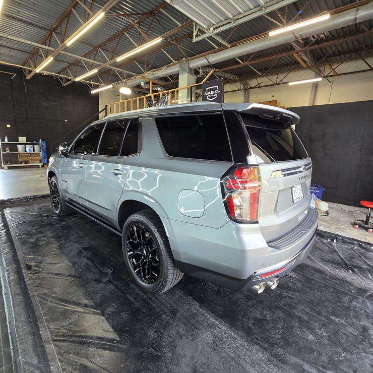 Gray SUV with black wheels in a garage, on a platform, under bright lights.