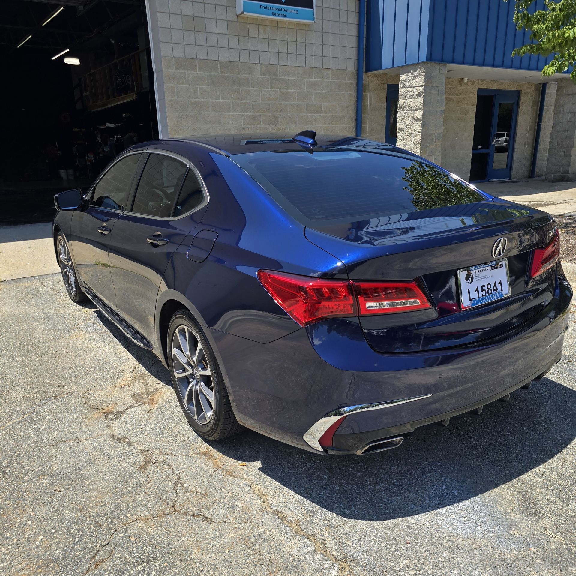 Blue Acura TLX sedan parked outside a building with tinted windows; sunlight.
